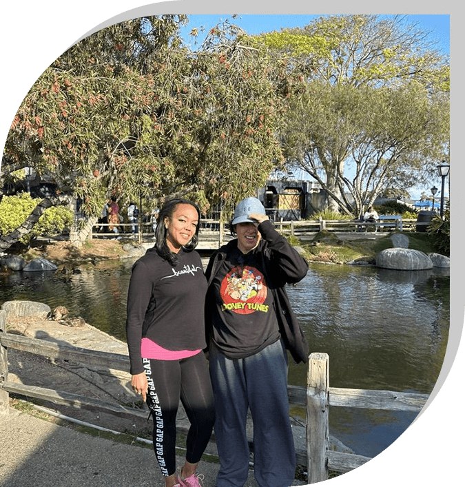 Two people standing next to a pond near trees.