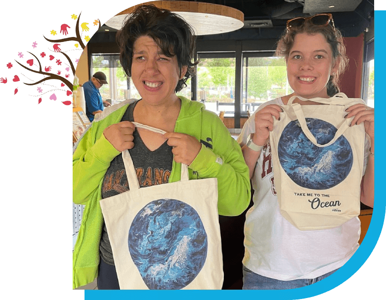 Two women holding up bags with a picture of the ocean.